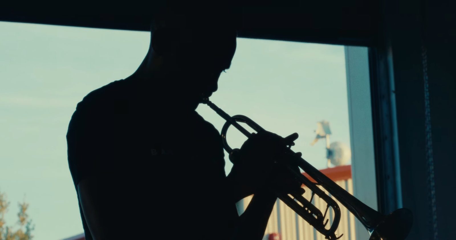 A trumpet player silhouetted against a window.